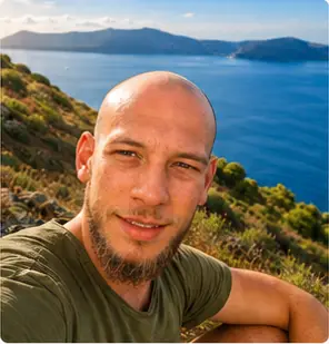 Alexandre Kallias souriant face à la caméra, la mer et la côte derrière lui